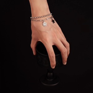 Detail of double-layer silver chain bracelet with smiley face and star pendants