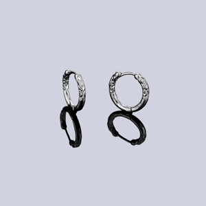 Macro detail of silver hoop earrings featuring irregular lava texture and mirror reflection