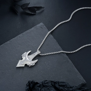 Macro shot of silver metal trident pendant with white enamel on black slate background