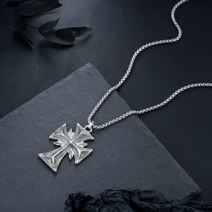 Gothic silver cross pendant on round box chain against dark industrial stone background