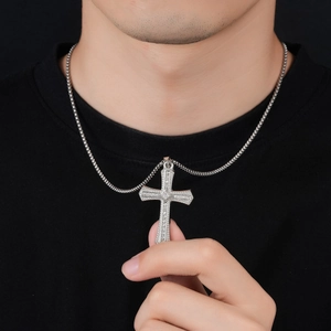 Gros plan du pendentif croix argenté avec cristaux scintillants porté par un modèle