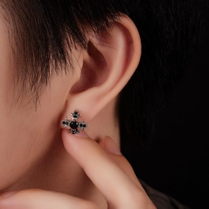 Macro close-up of a gothic cross earring with black zircon inlay on model's ear