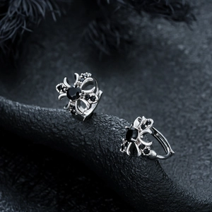 Macro view of silver cross earrings with black zircons on dark stone background