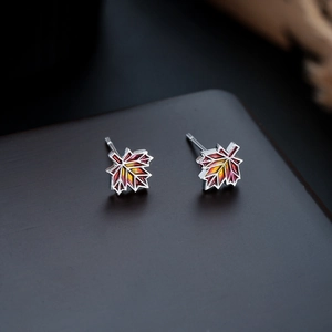 Detailed close-up of maple leaf earrings with vibrant red and orange enamel inlay