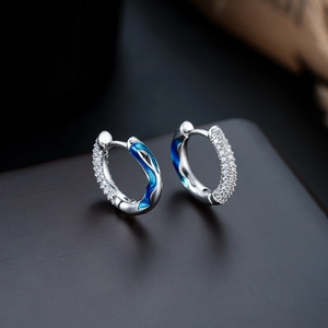 Detail of silver hoop earrings with micro-set zircons and deep blue enamel waves