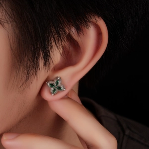 Macro view of four-leaf clover stud earring with green gemstones on a model's ear