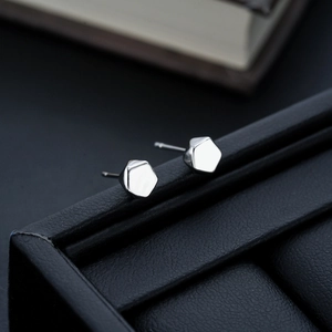 Macro shot of silver hexagonal geometric stud earrings on a black leather jewelry box