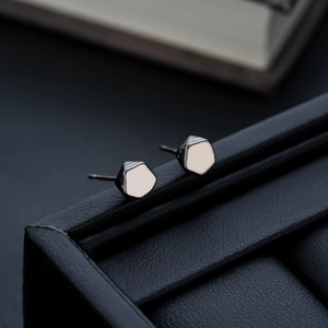 Detailed close-up of glossy black geometric stud earrings on a leather display case