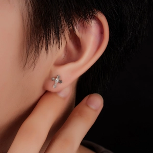 Close-up of silver cross stud earring with zircon stone inlay on a male model's ear