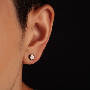 Close-up of a minimalist silver hexagonal stud earring worn on a male ear profile