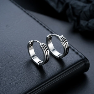 Detailed view of silver hoop earrings with black wave grooves on dark leather