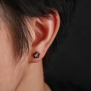 Macro side view of a star-shaped black stud earring with zircon on a person's ear