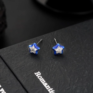 Close-up of blue enamel star stud earrings with central zircon on a black jewelry box