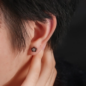 Close-up of star-shaped black stud earring with sparkling zircon on a person's ear