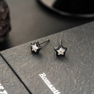 Close-up of black star earrings with clear zircon stones on a textured gift box