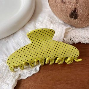 Detailed view of a green polka dot hair claw clip on a white lace fabric background
