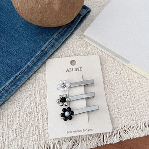 Gros plan de trois pinces à cheveux florales en métal blanc perle et argent sur carte