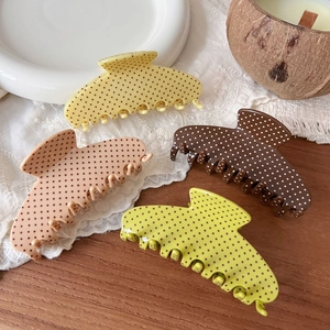 Close-up of four matte polka dot hair claw clips in neutral and green tones on a tray