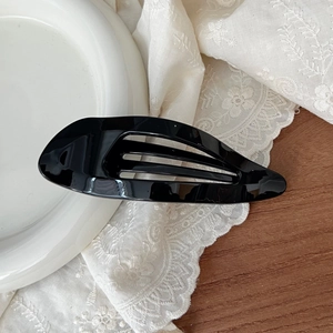 Detail of the glossy black hollow drop-shaped hair claw clip on a white ceramic tray
