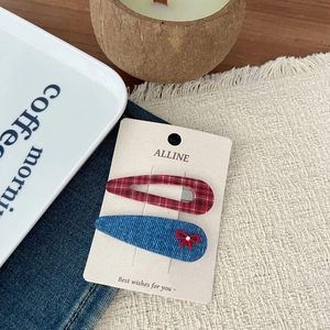 Detail view of retro plaid hair clip and blue denim bow clip on a beige brand card