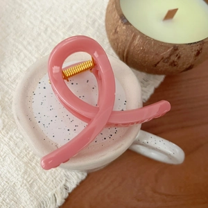 Pink minimalist twisted hair claw clip made of resin with golden spring on ceramic cup