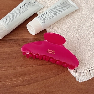 Elegant rose red acetate hair claw clip with golden logo on a natural wooden background