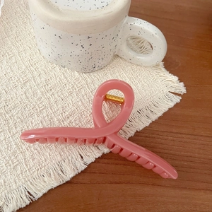Close-up of pink criss-cross hair claw clip on wooden table with ceramic mug