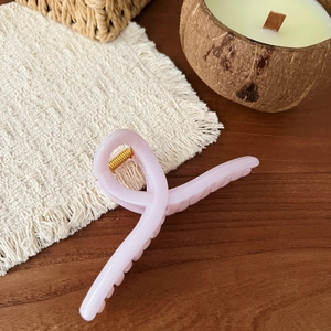 Detail of light pink resin hair claw clip with golden spring on wooden surface