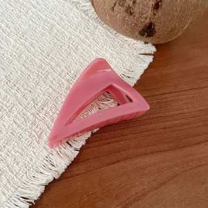 Detail view of a pink triangular hair claw clip on a rustic wooden table background