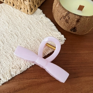 Detail of light pink bow hair claw clip with golden spring on cream fabric background