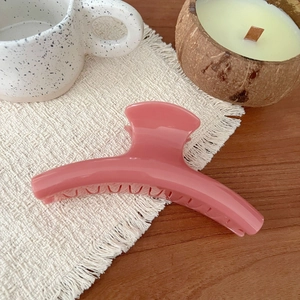 Close-up of a glossy plum pink claw clip on a textured beige fabric with cozy decor