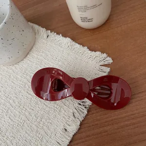 Nahaufnahme einer glänzenden weinroten Schleifen-Haarklammer auf beigem Fransenstoff