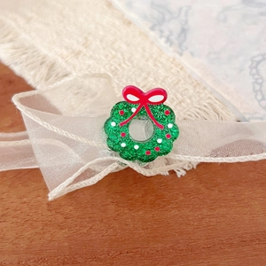 Green glitter Christmas wreath brooch with red bow on festive holiday background