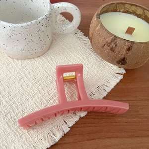 Close-up of matte pink plastic hair claw clip with golden spring on white fringe fabric