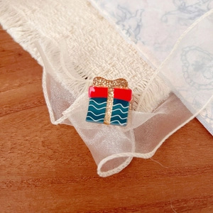 Detailed macro view of a red and blue enamel gift box brooch with golden glitter bow
