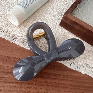 Detailed close-up of dark grey resin bow hair claw clip with a golden metal spring