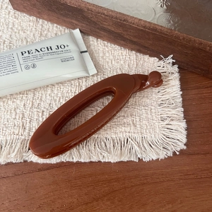 Detailed view of a sleek brown hollow banana hair clip on a bohemian white fringe mat