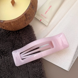 Detail of light pink rectangular hair claw clip with a glossy finish on textured fabric