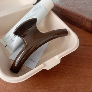 Close-up of a glossy brown resin hair claw clip in minimalist box on wooden background