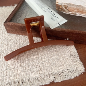 Detail of hollow rectangle sunset orange hair claw clip on soft cream fabric texture
