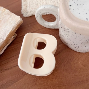 Gros plan d'une pince à cheveux en acétate crème avec un design minimaliste en forme de lettre B