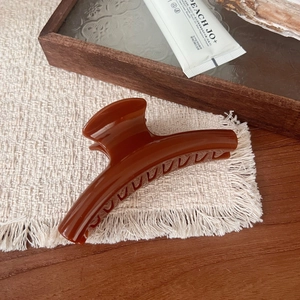 Detail view of a large glossy amber pumpkin hair claw clip on a rustic wooden tray
