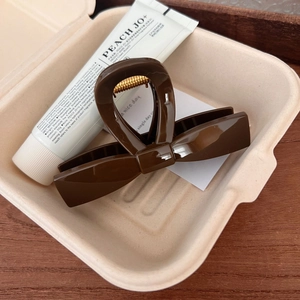 Detailed close-up of dark brown glossy bow hair claw clip with golden metal spring
