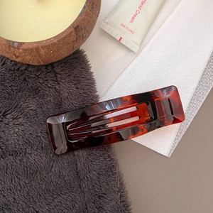 Detail of rectangular tortoise shell hair claw clip with warm amber pattern on plush background