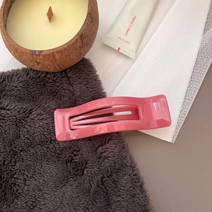 Glossy pink wavy hair claw clip displayed with lifestyle props on a soft fabric texture
