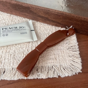 Detail of a brown resin banana hair clip with a minimalist bow design on a beige mat