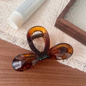 Detail view of amber resin bow hair claw clip with golden metal spring on white fabric