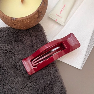 Detail of a burgundy rectangular hair claw clip on soft fabric with lifestyle props