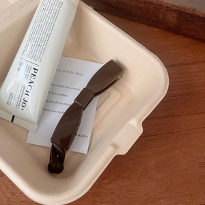 Close-up of a brown bow-shaped resin hair clip on a warm wooden surface background