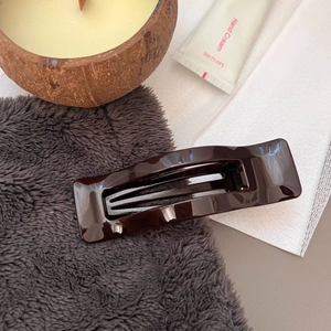 Detail of glossy chocolate brown hollow rectangular hair claw clip on cozy textured surface